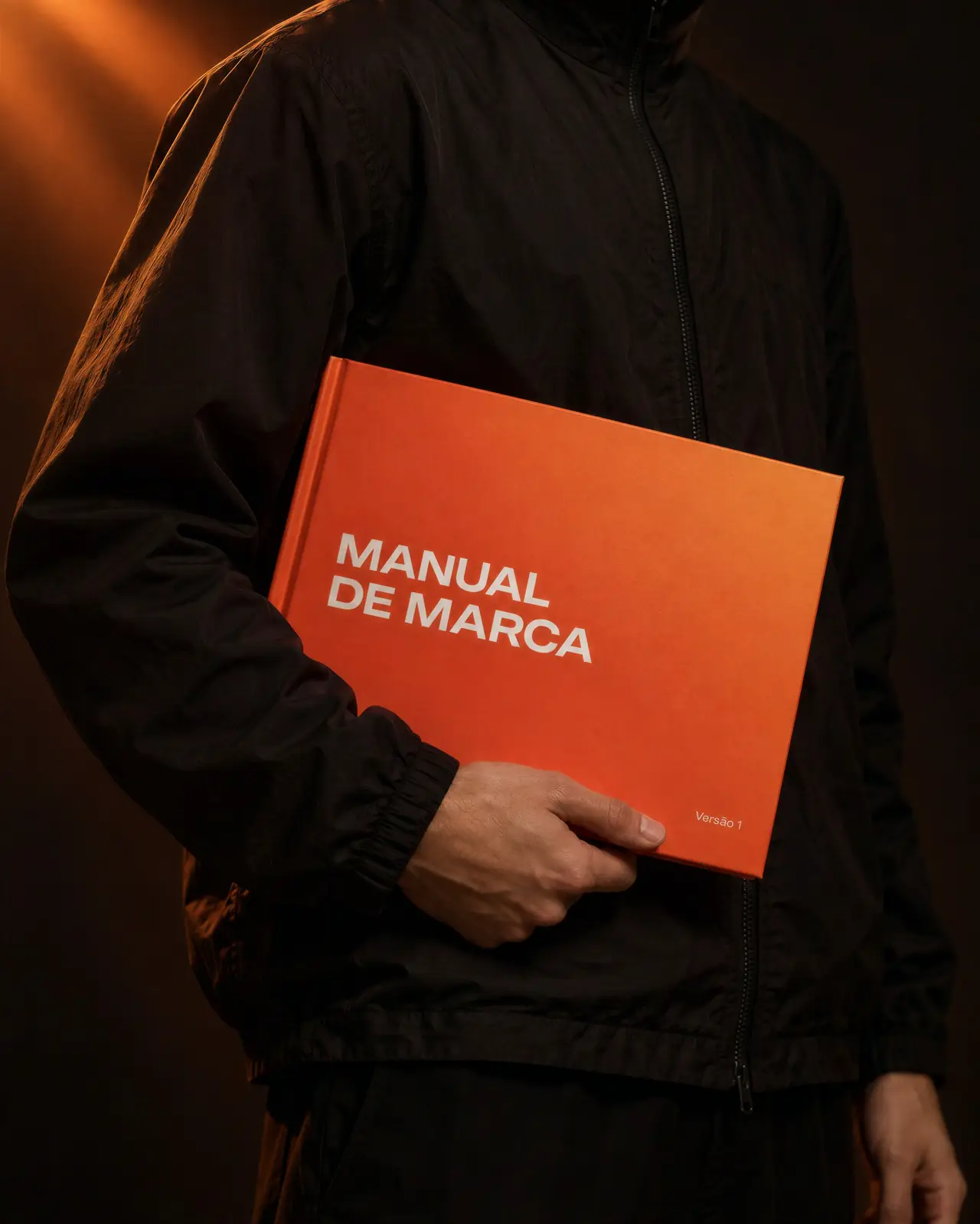 Manual de marca impresso, de capa laranja, na mão de uma pessoa de jaqueta preta