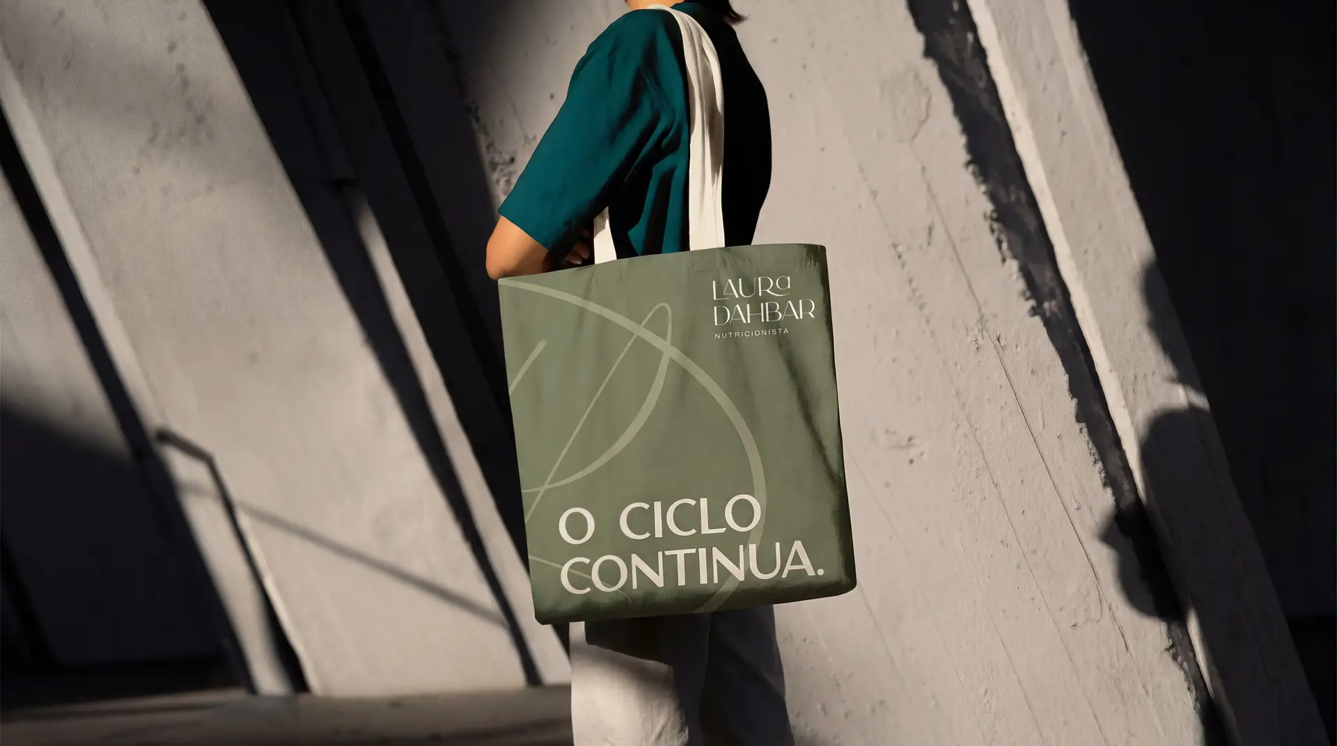 Ecobag verde com o monograma LD e a frase “O ciclo continua.” no ombro de uma mulher