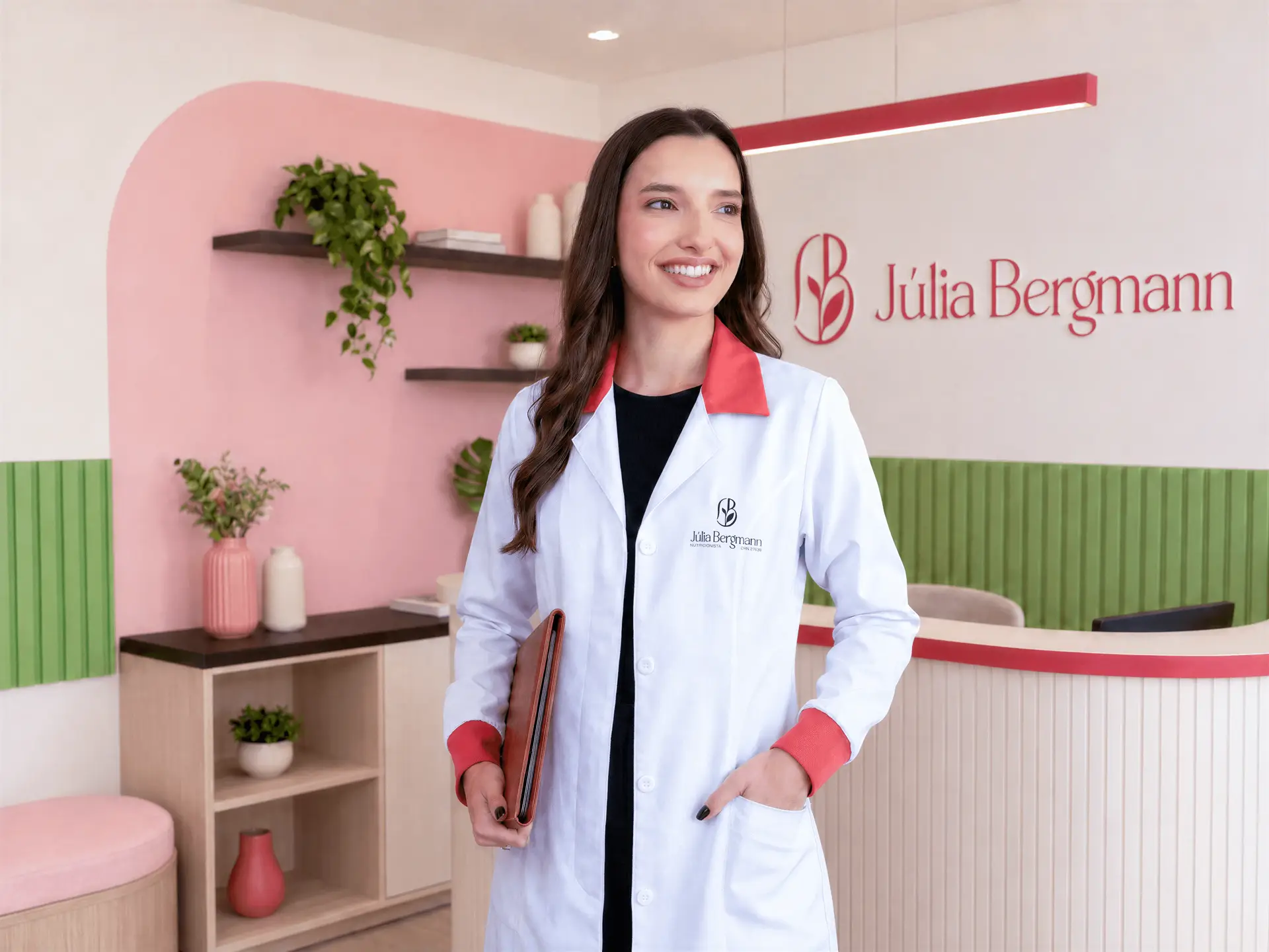 Júlia Bergmann de jaleco branco com gola vermelha, sorrindo na recepção de um consultório rosa e verde com o nome dela na parede.